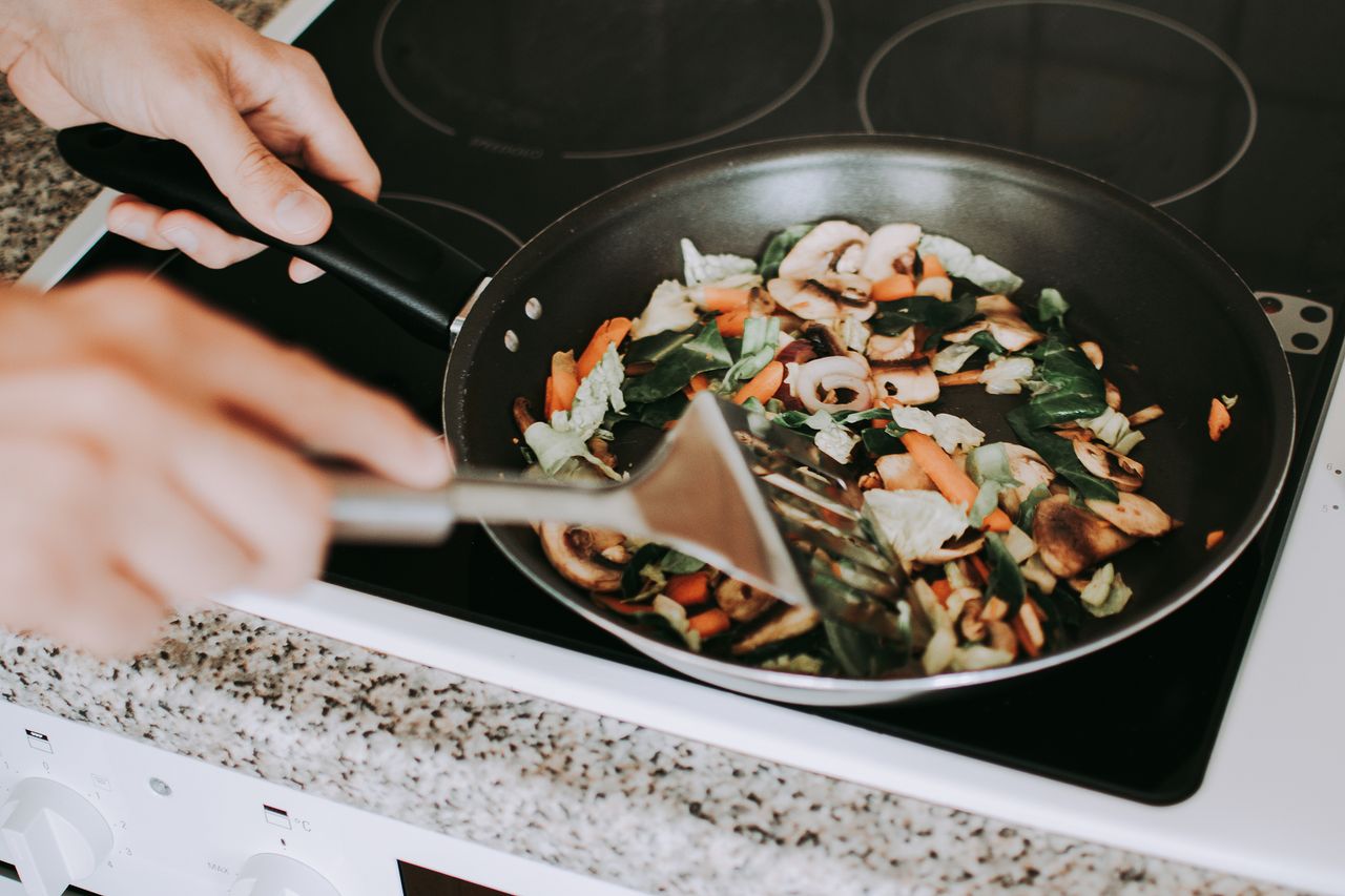 A person stirring vibrant vegetables in a frying pan on an electric stove.
